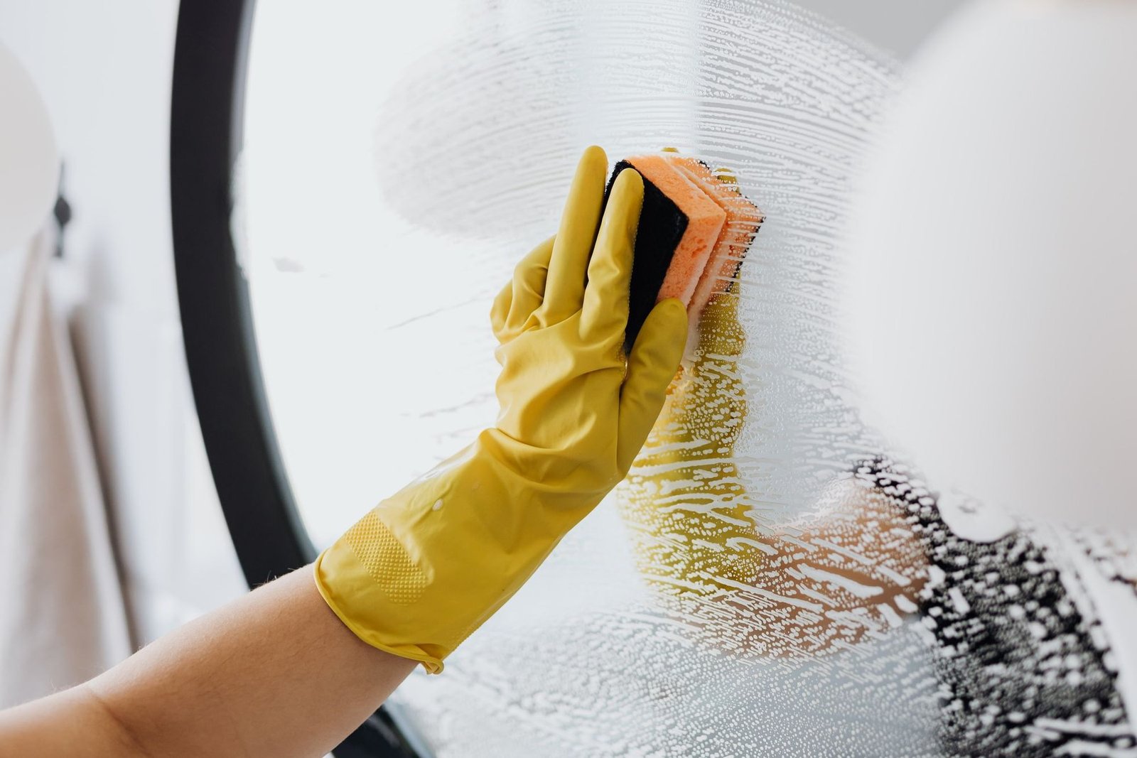 A gloved hand cleaning the glass door of a washing machine